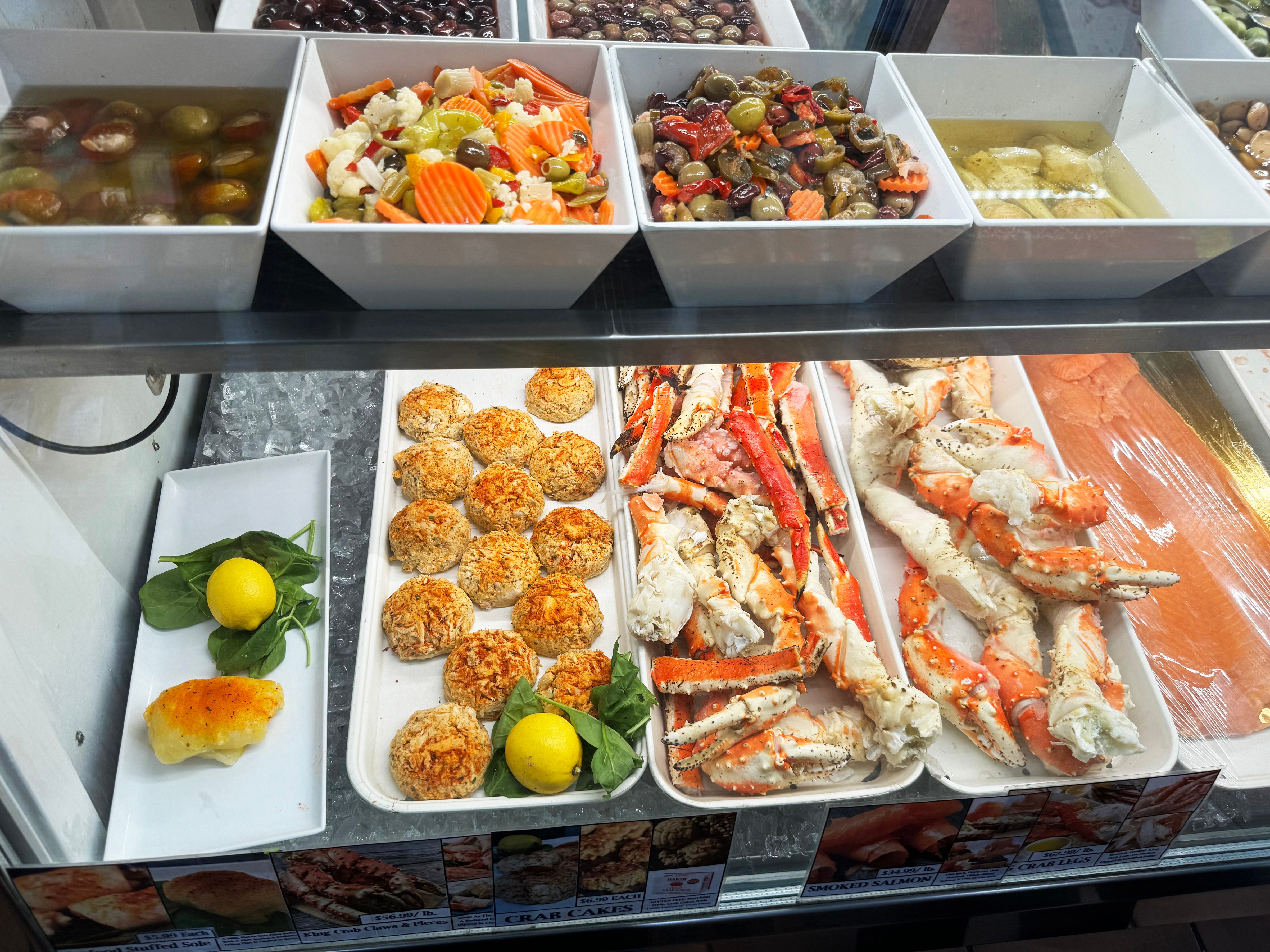 Blue cheese olives, giardiniera mixes, artichoke hearts (top shelf, front); assorted olives (top shelf, back), stuffed sole, crab cakes, king crab legs and smoked salmon (lower shelf).