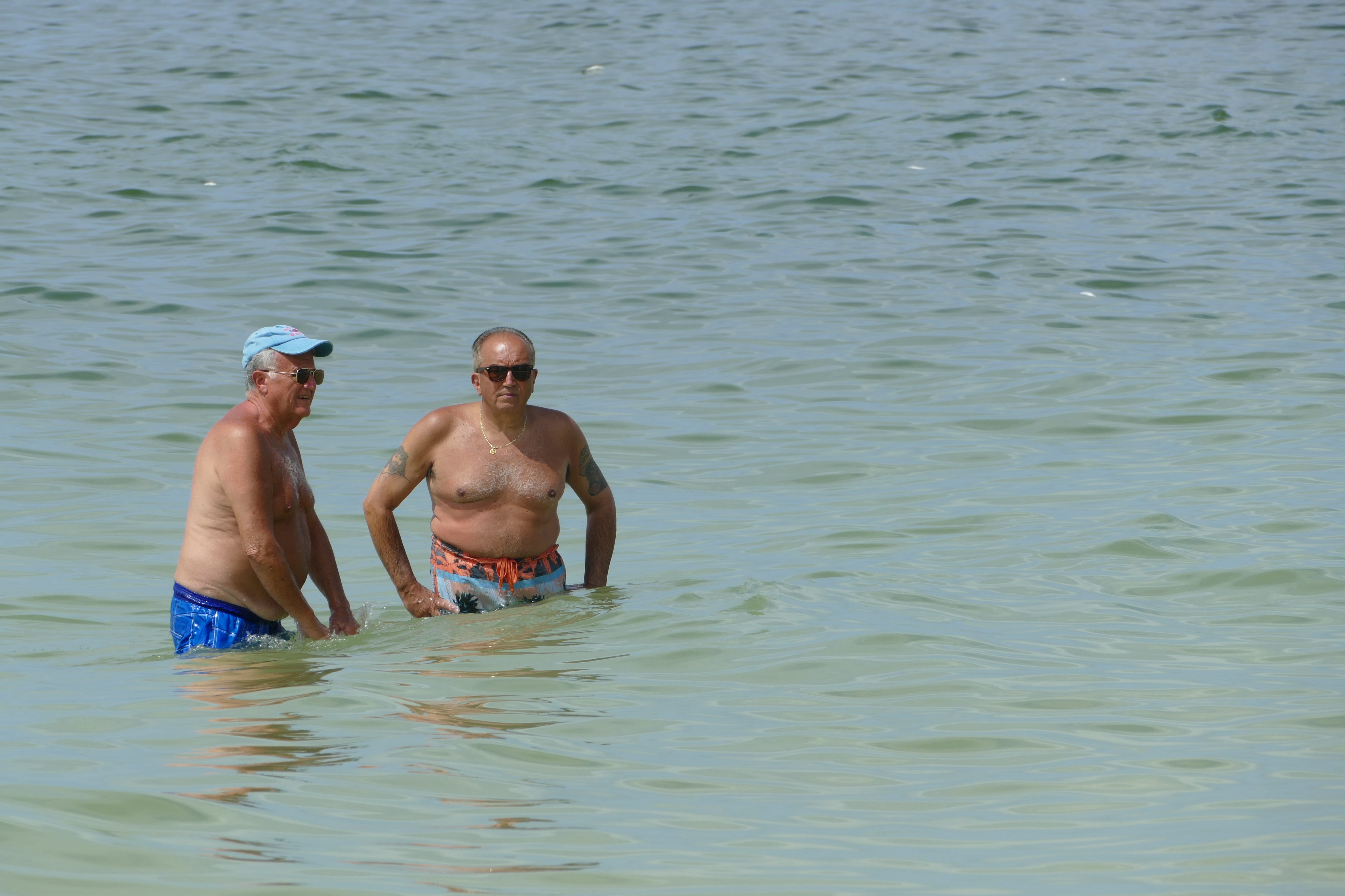 Two men enjoy the water of South Beach, Marco Island,  on Oct. 9. Dozens of dead fish washed ashore Wednesday on Marco Island as government agencies alerted of high levels of the organism that causes the red tide.